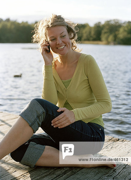 Eine Frau sitzt auf einer Mole in ein Handy zu sprechen.