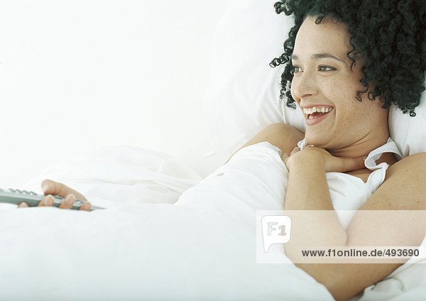 Frau im Bett liegend  Fernbedienung haltend