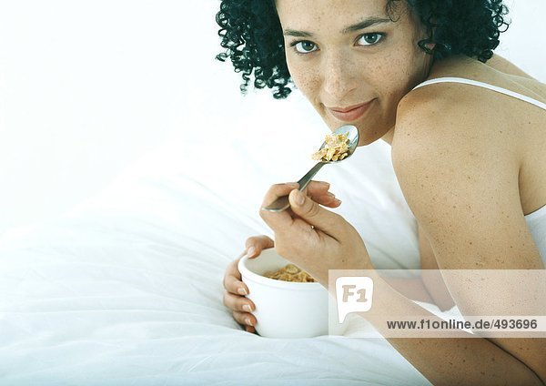 Frau liegt auf dem Bauch im Bett und isst Müsli.