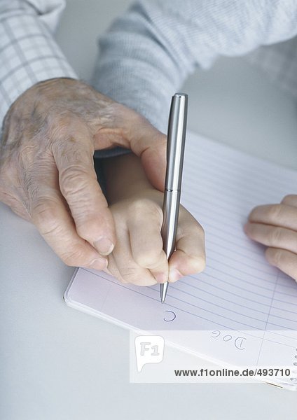 Hand der älteren Person  die das Kind führt und in ein Notizbuch schreibt.