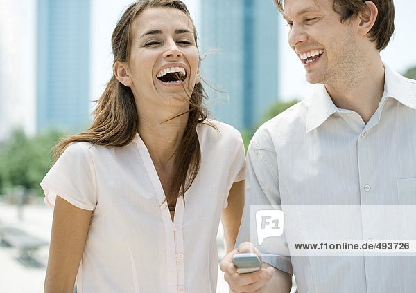 Young couple laughing as man holds cell phone