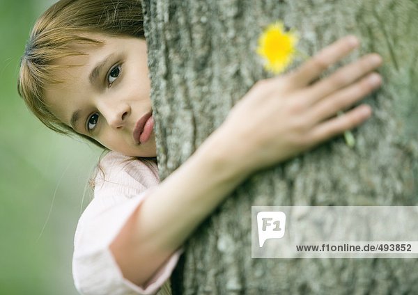Girl with arm around tree  holding flower