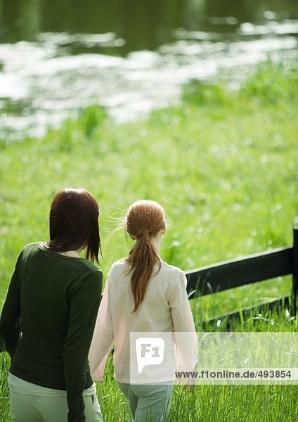 Woman and girl walking along wooden fence  pond in background