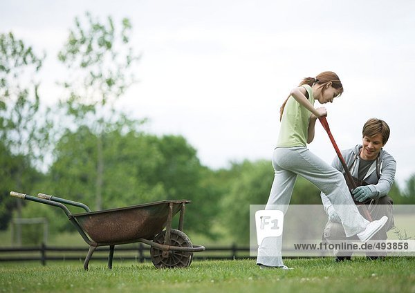 Girl digging in yard while man watches nearby