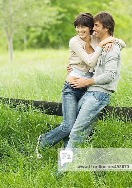 Young couple embracing and leaning against fence