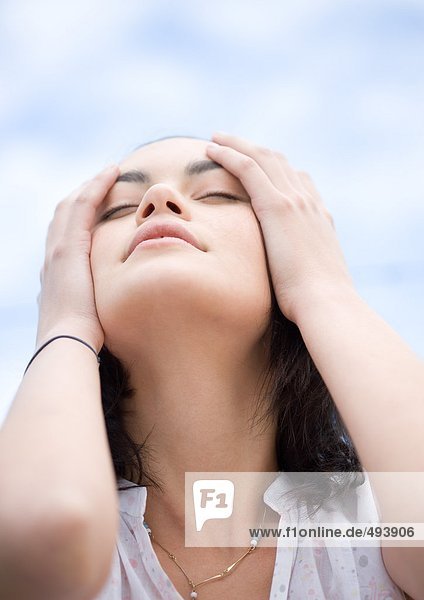 Frau mit den Händen auf der Seite des Kopfes  Tiefblick mit Himmel im Hintergrund