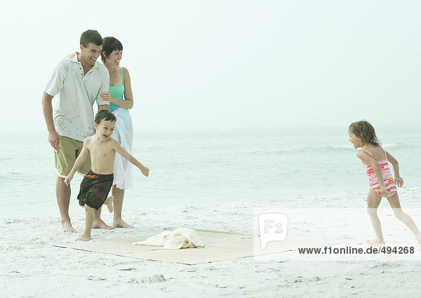 Familie am Strand  Kinder laufen um die Strandmatte herum