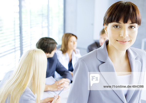 Businesswoman smiling at camera  meeting in background
