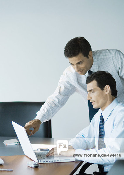 Businessman leaning over colleague's shoulder pointing at laptop screen
