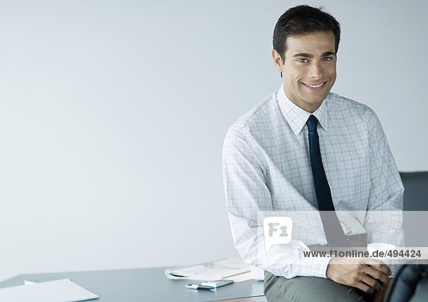 Geschäftsmann im Büro  hält Tasse und lächelt vor der Kamera