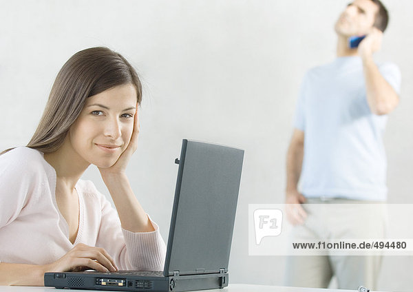 Woman using laptop while husband uses cell phone in background