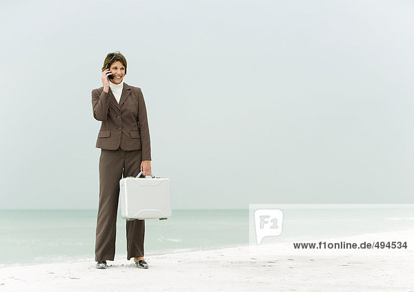 Geschäftsfrau  die am Strand steht und eine Aktentasche hält  mit dem Handy.