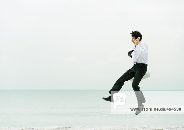 Businessman on beach  using cell phone and jumping