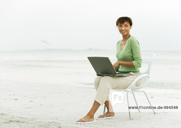 Frau am Strand  sitzend im Sessel mit Laptop