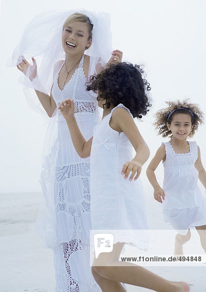 Zwei kleine Mädchen  die am Strand um die Braut rennen.