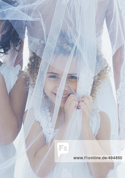 Little girl standing underneath bride's veil
