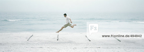 Mann springt über Baumstämme am Strand  Seitenansicht