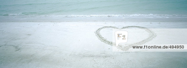 Child curled up inside heart shape on beach