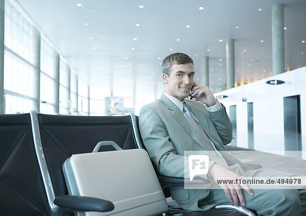 Geschäftsmann  der in der Flughafenlounge sitzt und sein Handy benutzt.