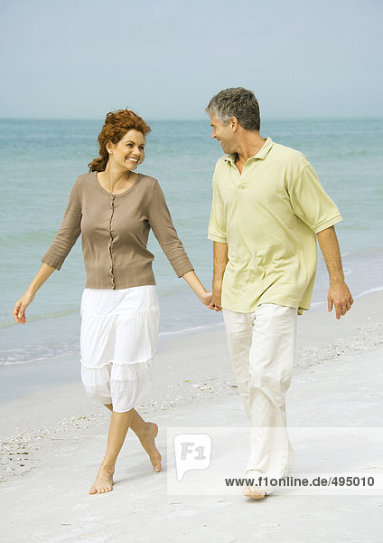 Mature couple walking barefoot on beach