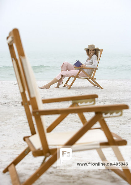 Frau im Strandkorb sitzend  leerer Stuhl im Vordergrund