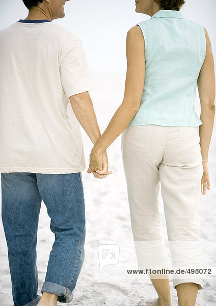 Mature couple walking hand in hand on beach  rear view