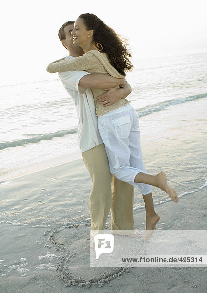 Paar in Herzform auf dem Strand stehend