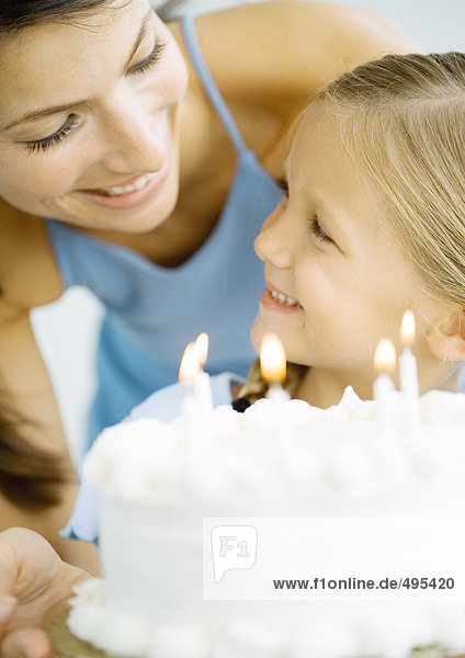Mutter und Tochter mit Geburtstagskuchen  die sich anlächeln.