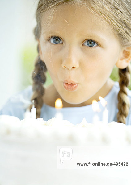 Kleines Mädchen beim Ausblasen von Kerzen auf Geburtstagskuchen