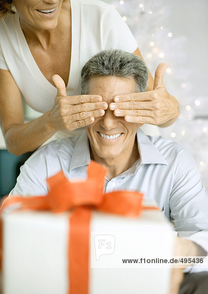 Frau bedeckt die Augen des Mannes  bevor sie ihm ein Weihnachtsgeschenk macht.