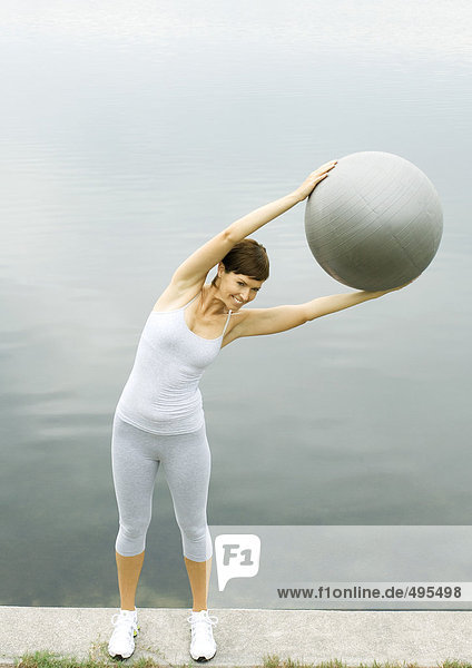 Woman exercising with fitness ball  next to lake