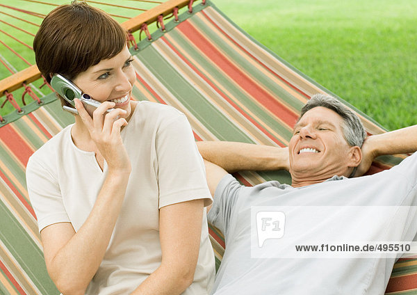 Mature couple lounging in hammock  woman using cell phone