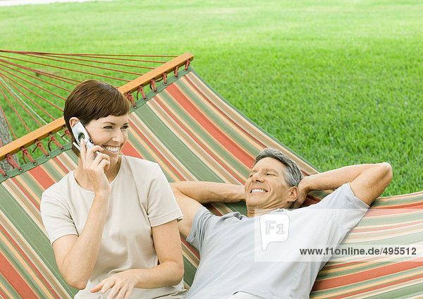 Mature couple lounging in hammock  woman using cell phone