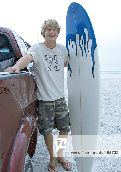 Surfer steht neben Pick-Up Truck mit Surfbrett