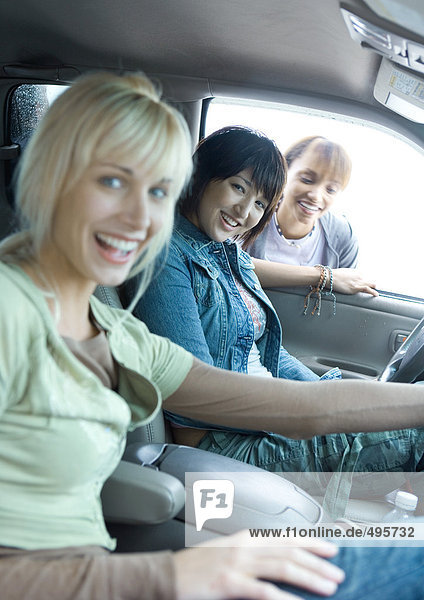 Zwei Frauen sitzen im Auto  die dritte Frau schaut durch das Autofenster.