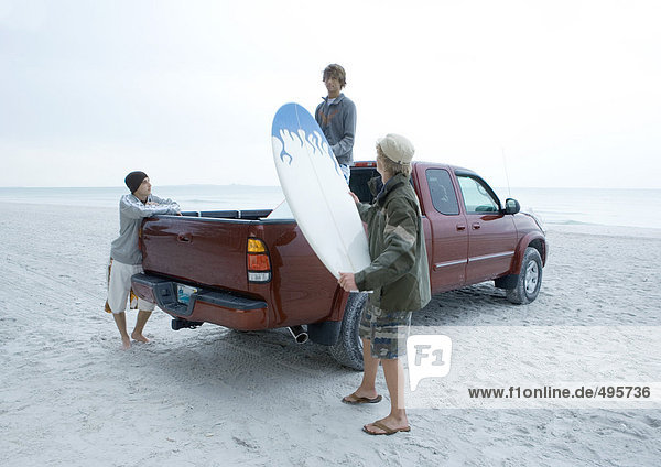 Drei Surfer nehmen das Surfbrett aus dem Pick-Up-Truck  am Strand.