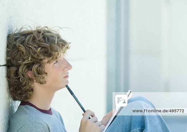 Teenager Junge sitzend mit Stift und Notizbuch  Seitenansicht