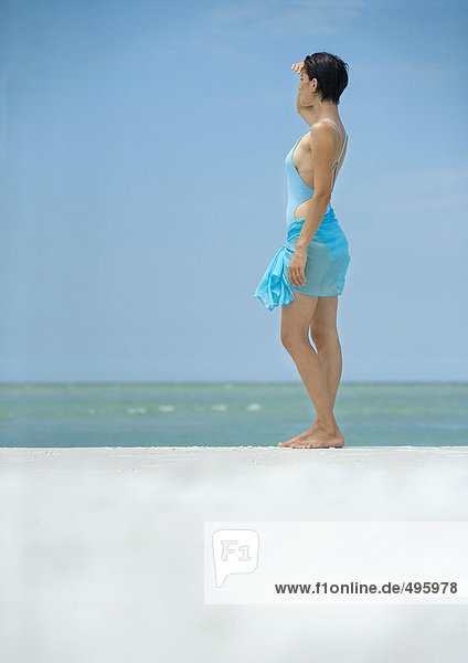 Frau am Strand stehend  mit Blick auf den Horizont