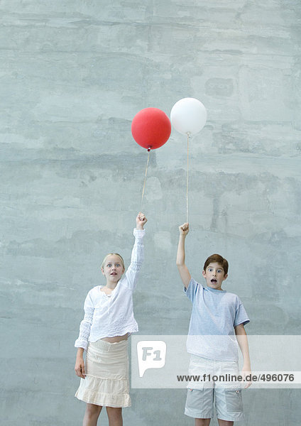 Zwei Kinder halten Luftballons  machen Gesichter