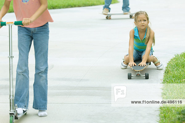Kinder auf Rollern und Skateboards in der Einfahrt