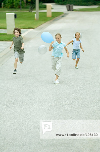 Kinder mit Luftballons  die durch die Wohnstraße laufen
