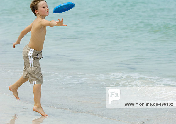 Junge wirft Frisbee am Strand