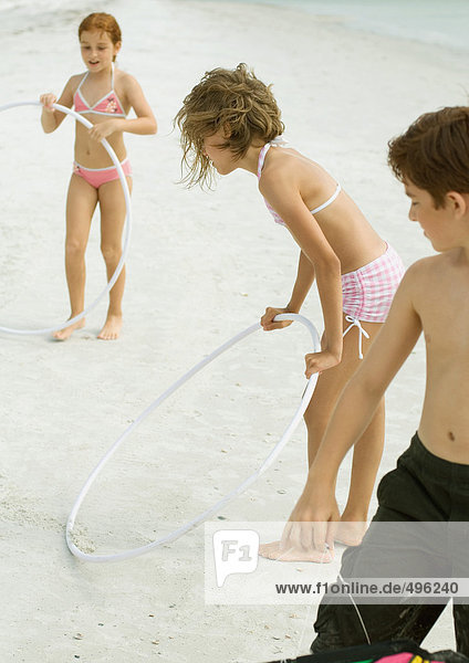 Kinder spielen mit Plastikreifen am Strand