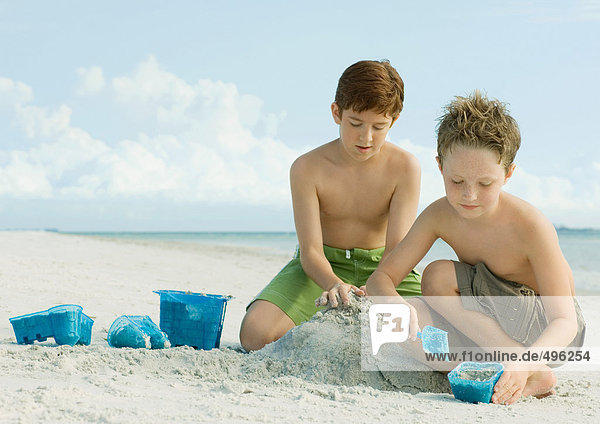 Jungen bauen Sandburg am Strand