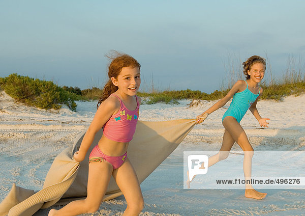 Two girls running on beach  holding blanket out in wind