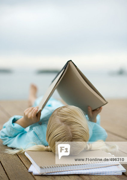 Girl reading book on dock