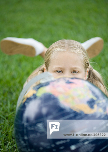 Mädchen auf Gras liegend mit Globus  mit Blick auf die Kamera