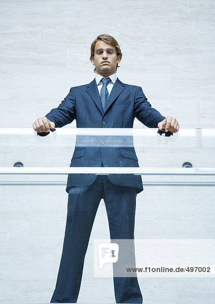Geschäftsmann stehend mit den Händen auf transparentem Geländer stehend  Portrait  Blickwinkel niedrig