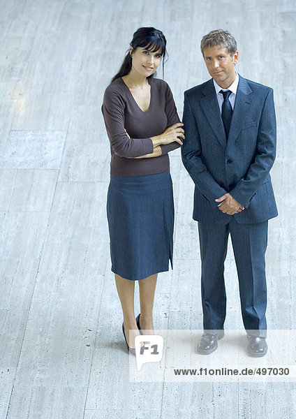 Businesswoman and businessman standing side by side  smiling at camera  portrait