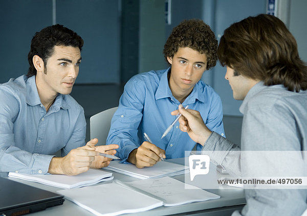 Drei männliche Kollegen am Tisch sitzen und über Dokumente reden